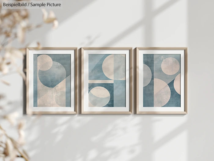 Triptych of abstract geometric art with blue and beige shapes in frames on a sunlit wall.