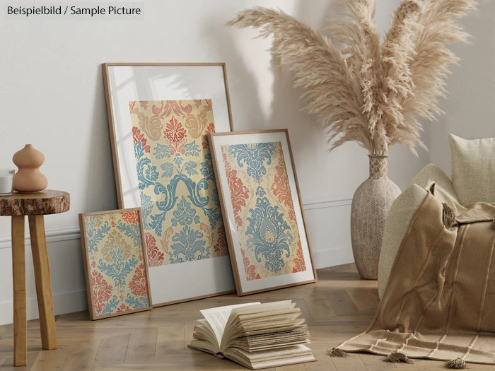 Cozy room with framed vintage pattern posters, dried pampas grass, and an open book on a wooden floor.