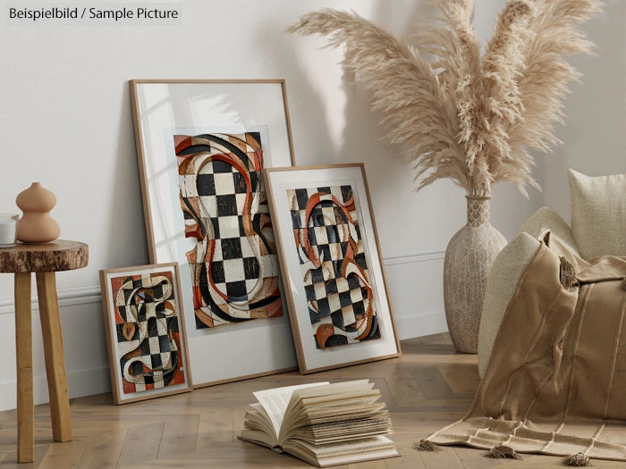 Framed abstract art pieces with geometric patterns on a wooden floor, next to pampas grass and cushions.