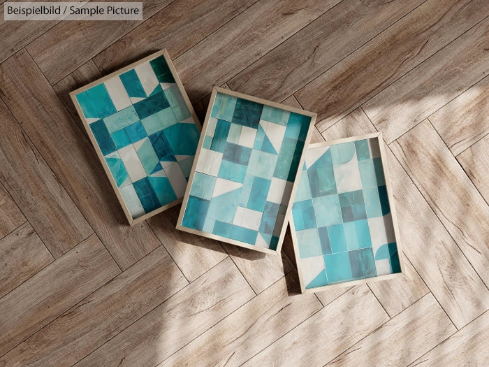 Three abstract teal and white geometric canvases on wooden floor.