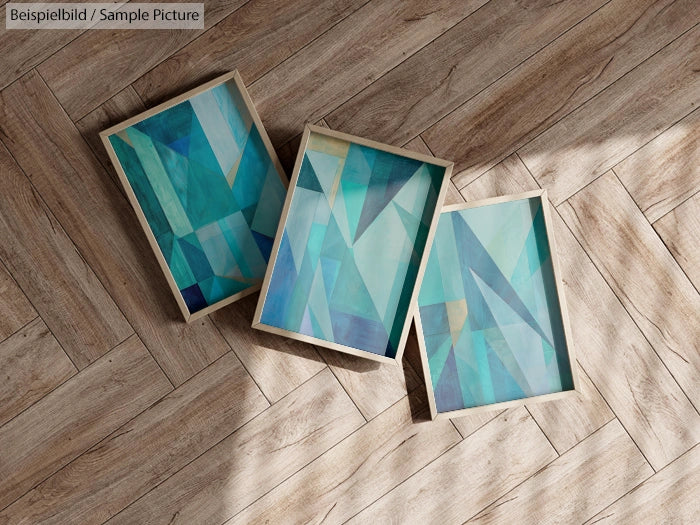 Three abstract blue and green geometric paintings on wooden floor.