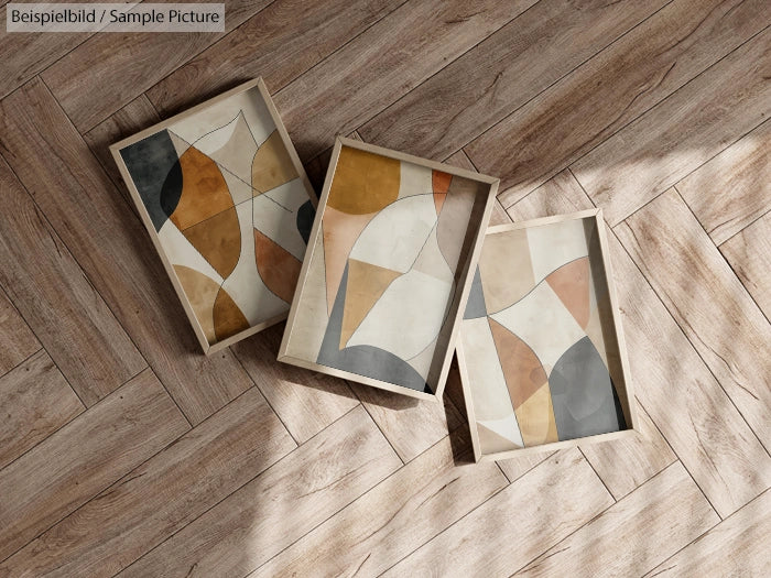 Three abstract art pieces with geometric shapes on wooden floor.