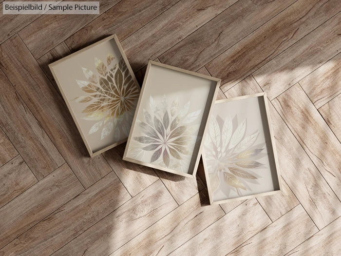 Three framed floral artworks with metallic leaves on wood-patterned floor in natural light.