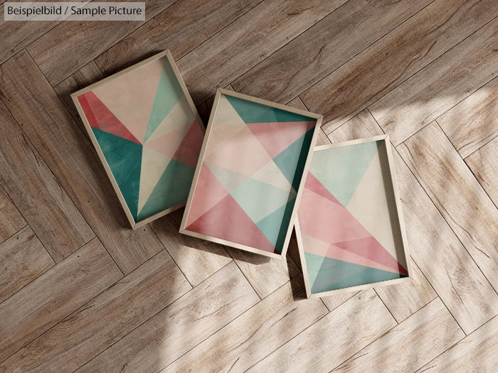 Three framed abstract geometric art pieces on wooden floor, featuring pink, green, and blue triangular patterns.