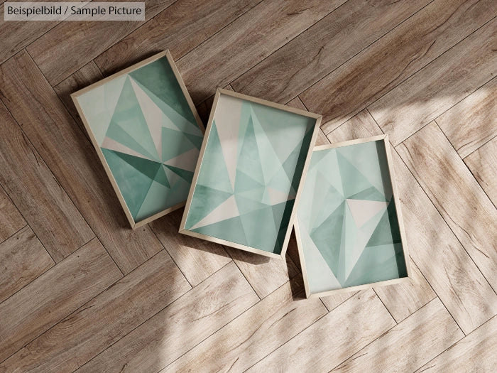 Three framed geometric prints with teal and gray patterns on wooden parquet flooring.