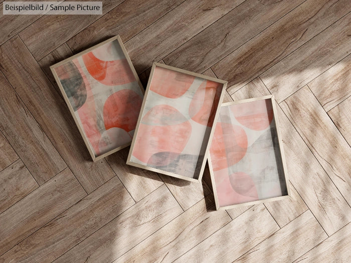 Three framed abstract prints with pink and orange circles on a wooden floor.