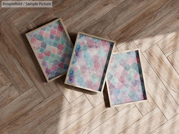 Three frames with pastel geometric patterns on a wooden floor surface.