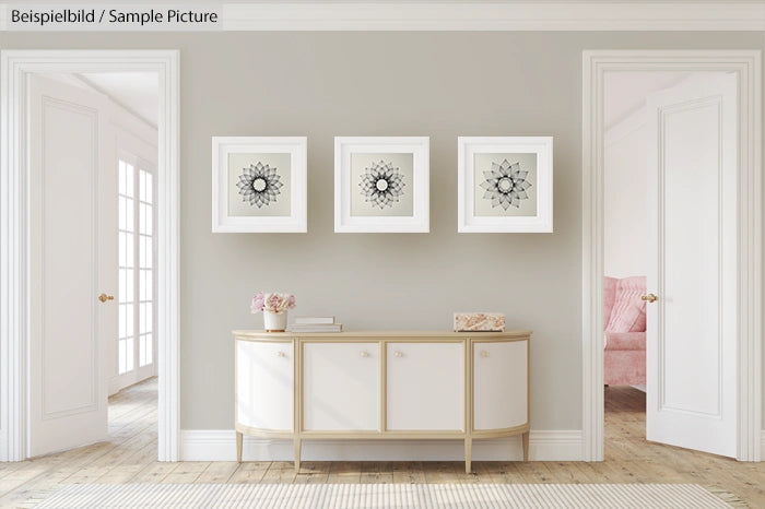 Minimalist hallway with a white console table, decorative flowers, and three framed geometric artworks on a grey wall.