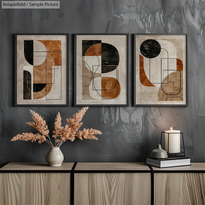 Modern geometric artwork trio above a wooden console with dried flowers and a lit candle.