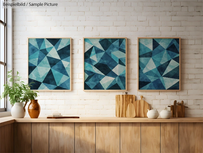 Three abstract blue geometric paintings on a brick wall above a wooden countertop with plants and kitchen utensils.