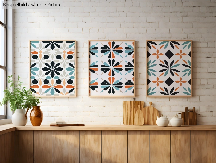 Three framed geometric pattern artworks on a white brick wall above a wooden counter with plants and pottery items.