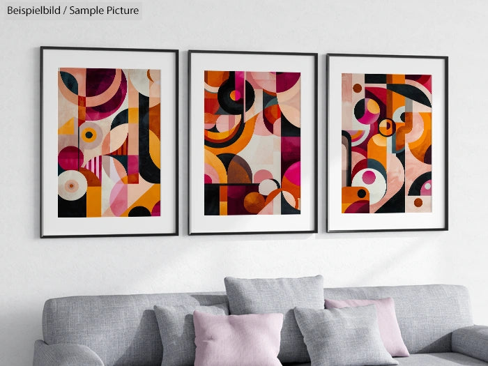 Three framed abstract artworks with bold geometric shapes and vibrant colors on a white wall above a gray sofa.