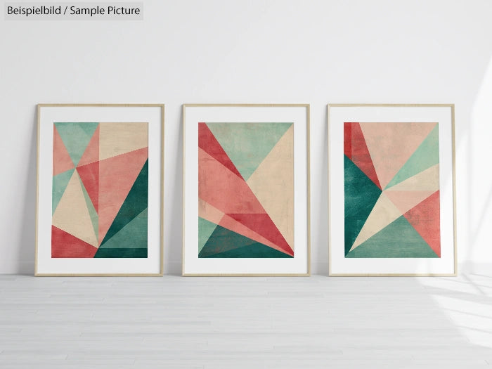 Three framed abstract geometric artworks with triangles in green, pink, and beige tones on a white wall.