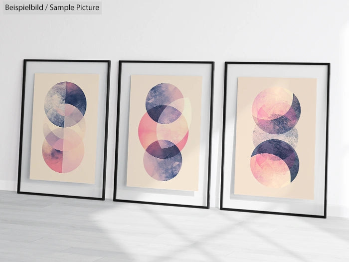 Framed abstract art prints with overlapping circles in pink, purple, and blue hues on a floor.