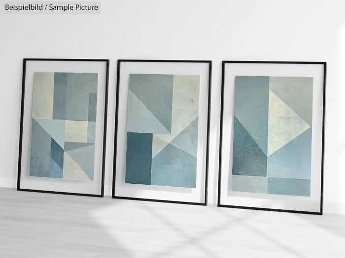 Three framed abstract geometric paintings in blue and green tones leaning against a white wall on a wooden floor.