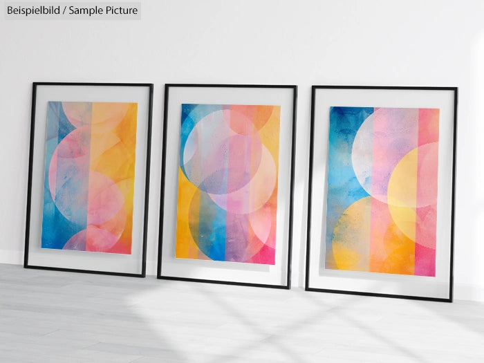 Three framed abstract paintings with overlapping circles in vibrant blue, pink, and yellow tones on a white wall.