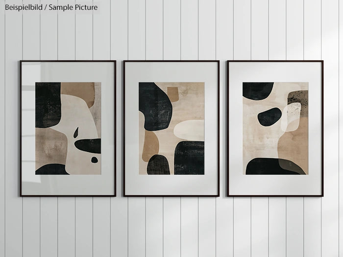 Trio of abstract modern art prints in black, beige, and white framed on a white-paneled wall.