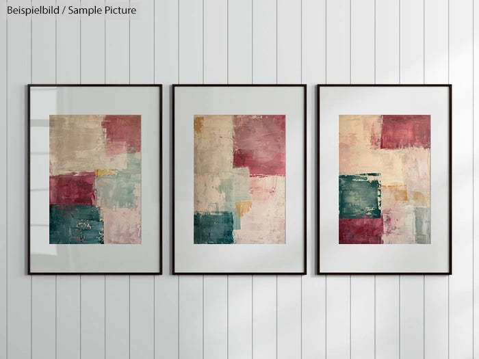 Triptych of abstract art with pink, teal, and beige squares in black frames on a wall with vertical lines.