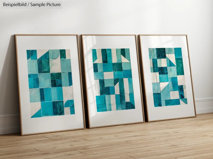 Three framed geometric abstract paintings with blue and white shapes on a wooden floor against a white wall.