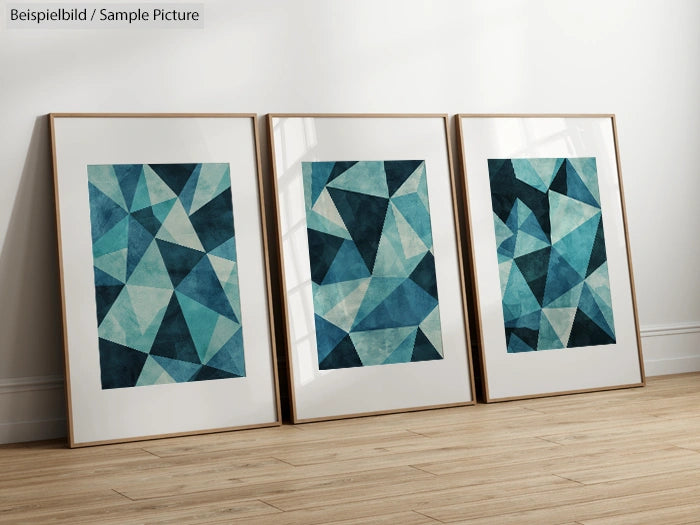 Triptych of abstract geometric paintings with blue and teal triangles in wooden frames on a wooden floor.