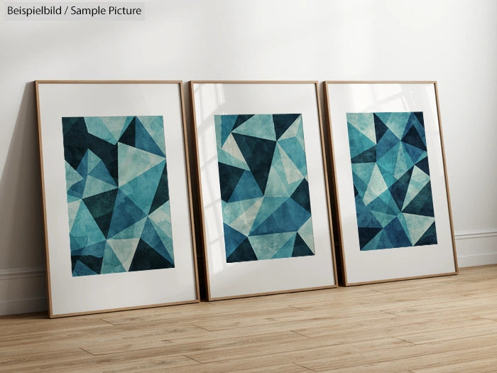 Set of three framed geometric abstract art pieces in blue and teal tones leaning against a white wall on wooden floor.