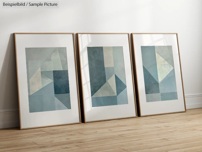 Three framed abstract geometric paintings with blue and gray tones, displayed on a wooden floor against a white wall.