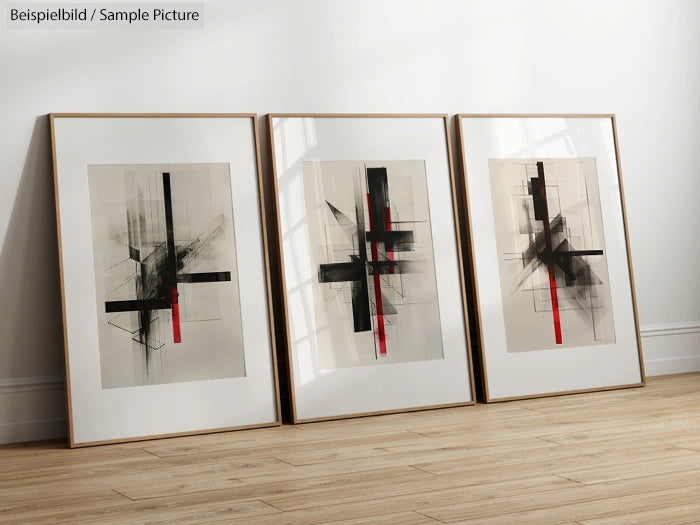 Three framed abstract paintings with black and red geometric patterns on a wooden floor against a white wall.