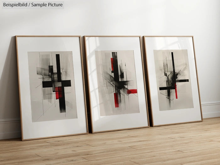 Three framed abstract art pieces with black and red geometric shapes, leaning against a white wall on wooden floor.