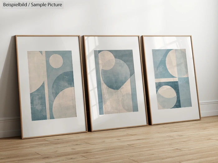 Three framed abstract prints with blue and beige geometric shapes on a wooden floor.