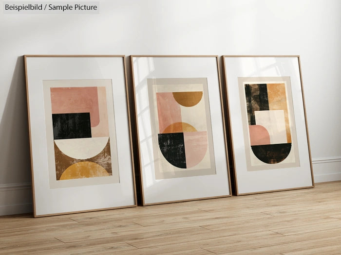 Three framed abstract art prints with geometric shapes on a wooden floor against a white wall.