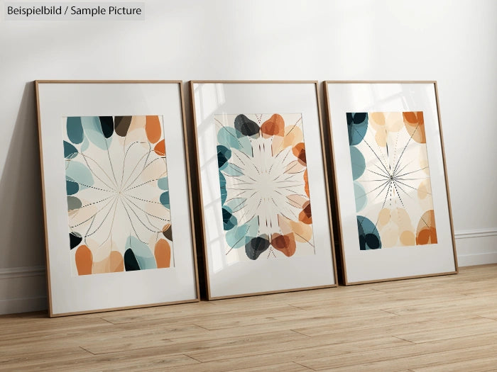 Three framed abstract art prints with geometric shapes in blue, orange, and beige tones, on a wooden floor.